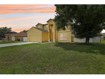 Two-story home with yellow stucco, attached garage, manicured lawn and mature trees at sunset at 670 Bluebill Ct, Poinciana, FL 34759