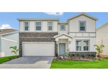 Two-story home with stone accents, a well-maintained lawn, and a paved driveway leading to a two-car garage at 3082 Mahalo Dr, Davenport, FL 33897