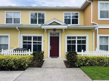 Charming yellow townhome featuring a red front door, white picket fence and lush landscaping at 4010 Santa Maria Dr # 106, Kissimmee, FL 34741