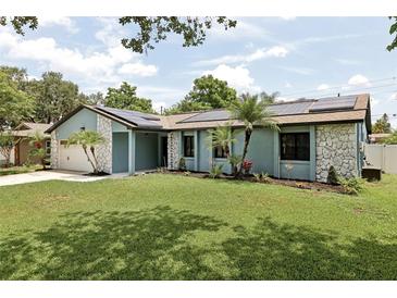 Charming single-story home with a manicured lawn, accented by stone details and solar panels on the roof at 1360 Gladiolas Dr, Winter Park, FL 32792