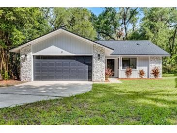 Charming home featuring stone accents, a gray garage door, and a well-maintained front lawn at 2 Rollingwood Trl, Deland, FL 32724