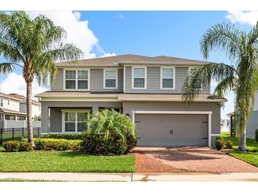 Two-story home with a gray exterior, manicured landscaping, palm trees, and a brick driveway leading to an attached garage at 2431 Tudor Rose Dr, Sanford, FL 32773