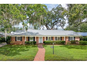Charming brick home featuring a manicured lawn, brick walkway, and mature trees draped with Spanish moss at 2500 Lake Shore Dr, Orlando, FL 32803