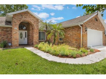 Charming brick home featuring an arched entryway, manicured lawn, and lush landscaping at 109 Hunter Point Ct, Debary, FL 32713