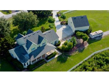 Expansive aerial view of a large, light green house with a detached garage, pool, and green lawn at 10809 Arrowtree Blvd, Clermont, FL 34715