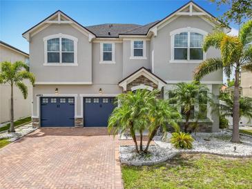 Elegant two-story home with a manicured lawn, brick driveway, and two-car garage, enhanced by lush palm trees at 4993 Southlawn Ave, Orlando, FL 32811