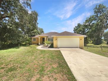 Charming yellow home featuring a spacious front yard, attached two-car garage, and meticulously landscaped entry at 10170 Se 106Th Ln, Belleview, FL 34420