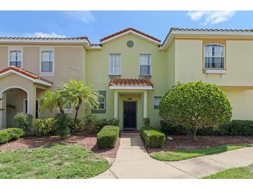 Charming two-story townhome with colorful exterior, featuring tiled roof, manicured lawn, and walkway to the front door at 214 Monroe Cir, Davenport, FL 33896