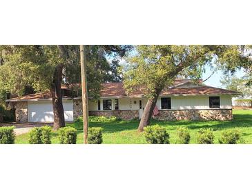 Charming single-story home with stone accents, a manicured lawn, and a welcoming two-car garage at 10012 Lake Louisa Rd, Clermont, FL 34711
