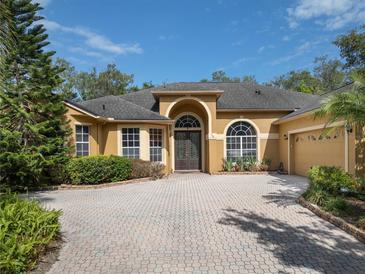 Inviting home featuring a brick driveway, two-car garage, lush landscaping, and an arched entryway at 140 Seville Chase Dr, Winter Springs, FL 32708