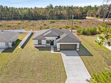 Stunning aerial view of home featuring a spacious lawn, gray roof, brown garage door, and long driveway at 16730 Sw 50Th Cir, Ocala, FL 34473