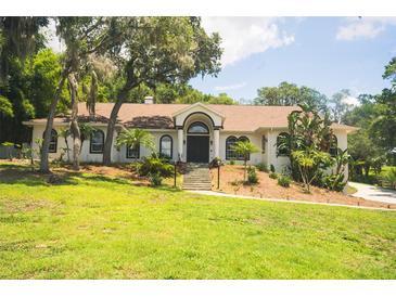 Charming single-story home with arched windows, landscaped yard, and mature trees at 16400 Lakeshore Dr, Minneola, FL 34715