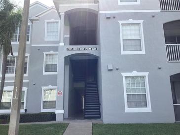 A light grey condominium building with an open walkway in a lush, green community at 2305 Butterfly Palm Way # 304, Kissimmee, FL 34747