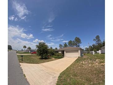 Single-story home featuring an attached two-car garage, manicured lawn, and a long driveway at 3381 Sw 129Th Loop, Ocala, FL 34473