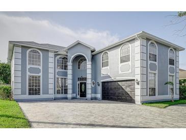 Spacious two-story home with an elegant grey exterior, large windows, and a patterned brick driveway at 224 Hammock Dunes Pl, Orlando, FL 32828