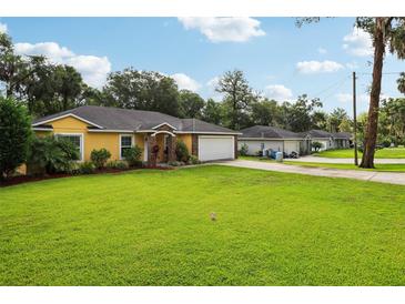 Charming yellow house featuring a well-manicured lawn, lovely landscaping, and an attached two-car garage at 395 Alcazar Ave, De Leon Springs, FL 32130