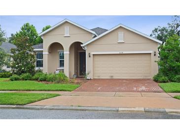 Charming beige home featuring a brick driveway, arched entryway, and well-maintained landscaping at 2339 Jernigan Loop, Kissimmee, FL 34746