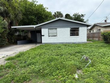 Exterior view of a single story home with a white brick facade and an attached carport with overgrown landscaping at 508 S Caroline St, Daytona Beach, FL 32114