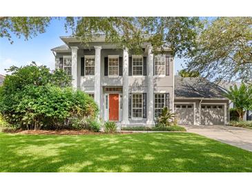 Classic two-story home boasts stately pillars, a well-manicured lawn, an orange front door, and mature landscaping at 11425 Claymont Cir, Windermere, FL 34786