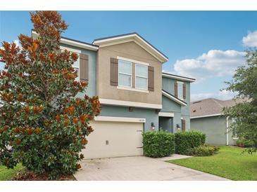 Two story home with a beige two-car garage, manicured landscaping, and a decorative tree on the front lawn at 16440 Centipede St, Clermont, FL 34714