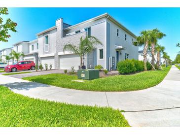 Modern townhome with a two-car garage, stone accents, lush landscaping, and a red car parked in driveway at 224 Nine Iron Dr, Davenport, FL 33896
