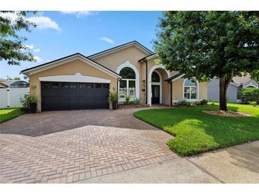 Charming tan home with a two-car garage, arched windows, and a brick driveway and walkway at 1008 Soldier Creek Ct, Oviedo, FL 32765