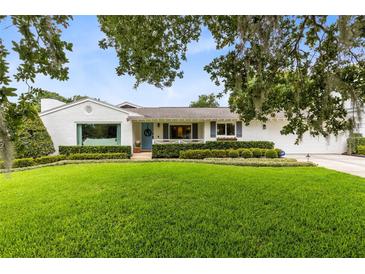 Charming single-story home with a well-manicured lawn, mature trees, and a welcoming blue front door at 609 Langholm Dr, Winter Park, FL 32789