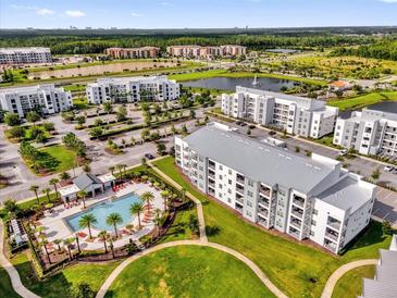 Stunning aerial view of a community with a resort-style pool, lush landscaping, and modern apartment buildings near a lake at 3180 Paradox Cir # 304, Kissimmee, FL 34746