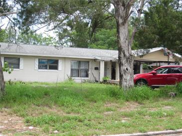 Modest single-story home with light exterior, mature trees, and driveway with covered parking at 2200 Queensway Rd, Orlando, FL 32808