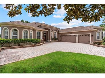 Elegant single-story home featuring a paver driveway, three-car garage, arched windows, and well-maintained landscaping at 23538 Valderama Ln, Sorrento, FL 32776