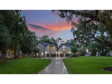 Stately home featuring dual garages, mature trees, lush landscaping and a brick paved driveway at dusk at 2652 Lake Howell Ln, Winter Park, FL 32792