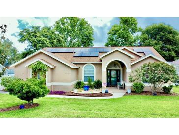 Charming single-story home featuring well-manicured lawn, mature trees, and solar panels on the roof at 14723 Pine Cone Trl, Clermont, FL 34711