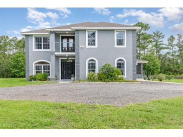 Two story home with grey stucco, manicured landscaping, black front door, and a circular gravel driveway at 32125 Wekiva Pines Blvd, Sorrento, FL 32776