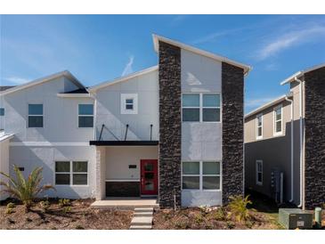 Stylish two-story home with a modern facade, stone accents, and a vibrant red front door at 1070 Splash Shot Pl, Davenport, FL 33896