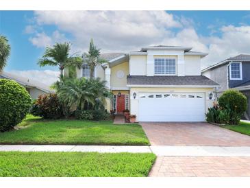 Charming two-story home with a well-manicured lawn, tropical plants, and a brick driveway at 2205 Wyndam Way, Kissimmee, FL 34743