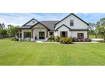 Charming farmhouse exterior with lush lawn, black roof, white siding, and welcoming front porch at 27071 Moss View Dr, Tavares, FL 32778