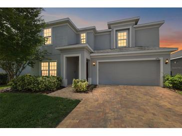 Charming two-story home showcasing a brick driveway, attached two-car garage, and landscaped front yard at dusk at 1292 Cavender Creek Rd, Minneola, FL 34715