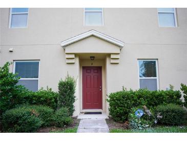 Inviting front entrance with a classic red door, trimmed bushes, and muted neutral stucco at 3569 Seneca Club Loop # 13, Orlando, FL 32808
