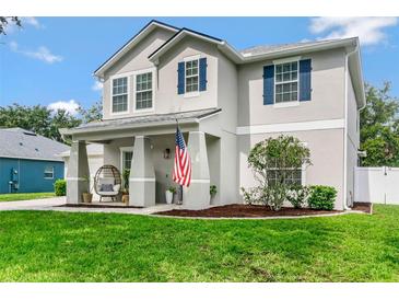 Charming two-story home with a well-manicured lawn, blue shutters, and inviting front porch with comfortable seating at 486 Shirley Dr, Apopka, FL 32712