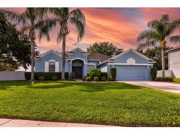 Charming blue home boasts a well-manicured lawn, lush landscaping, and swaying palm trees at 2237 Wintermere Pointe Dr, Winter Garden, FL 34787
