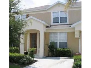 Inviting two-story townhome featuring a covered entry, tan stucco exterior, and well-maintained landscaping at 7682 Sir Kaufmann Ct, Kissimmee, FL 34747