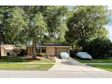 Cozy home with a large, mature tree in the front yard and a covered vehicle in the driveway at 34 W Bob White St, Apopka, FL 32712