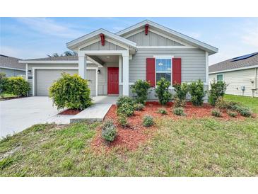 Charming single-story home with a red front door, grey siding, and a well-maintained lawn with tidy landscaping at 584 S Andrea Cir, Haines City, FL 33844