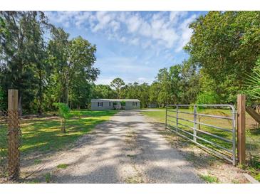 Gated property with a long gravel driveway leading to a charming single-story home surrounded by mature trees at 18166 Lynbrook Rd, Orlando, FL 32820