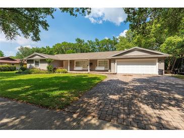Charming single-story home featuring a manicured lawn, brick driveway, and inviting porch swings at 1111 Pinar Dr, Orlando, FL 32825