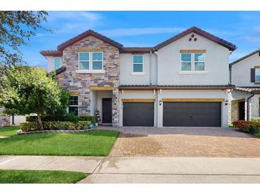 Beautiful two-story home featuring stone accents, manicured lawn, and a brick driveway leading to a three-car garage at 14124 Dove Hollow Dr, Orlando, FL 32824