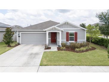 Charming single-story home with well-manicured lawn, gray siding, and a pop of color from the red front door and shutter at 561 Andrea S Cir, Haines City, FL 33844