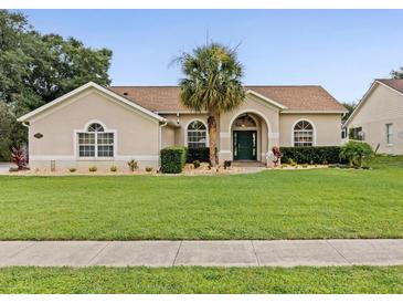 Charming single-story home boasts a lush lawn, manicured landscaping, and a welcoming entrance with a stately palm tree at 14322 Pine Cone Trl, Clermont, FL 34711