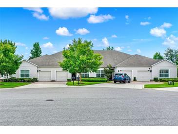 Well-manicured front exterior of neutral colored home with three garage doors, green trees and lawn and blue sky at 3210 Sonesta Ct # B, Clermont, FL 34711