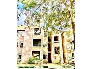Exterior of a multi-story building with brick and siding, surrounded by trees and landscaping at 5500 Devonbriar Way # 202, Orlando, FL 32822